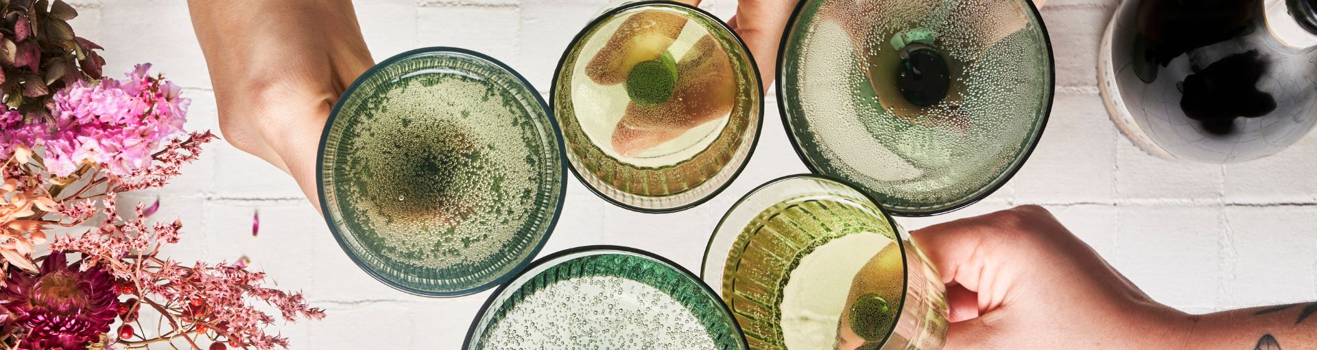 Gläser aus grünem Glas in unterschiedlichen Formen, gefüllt mit Sekt, stoßen an