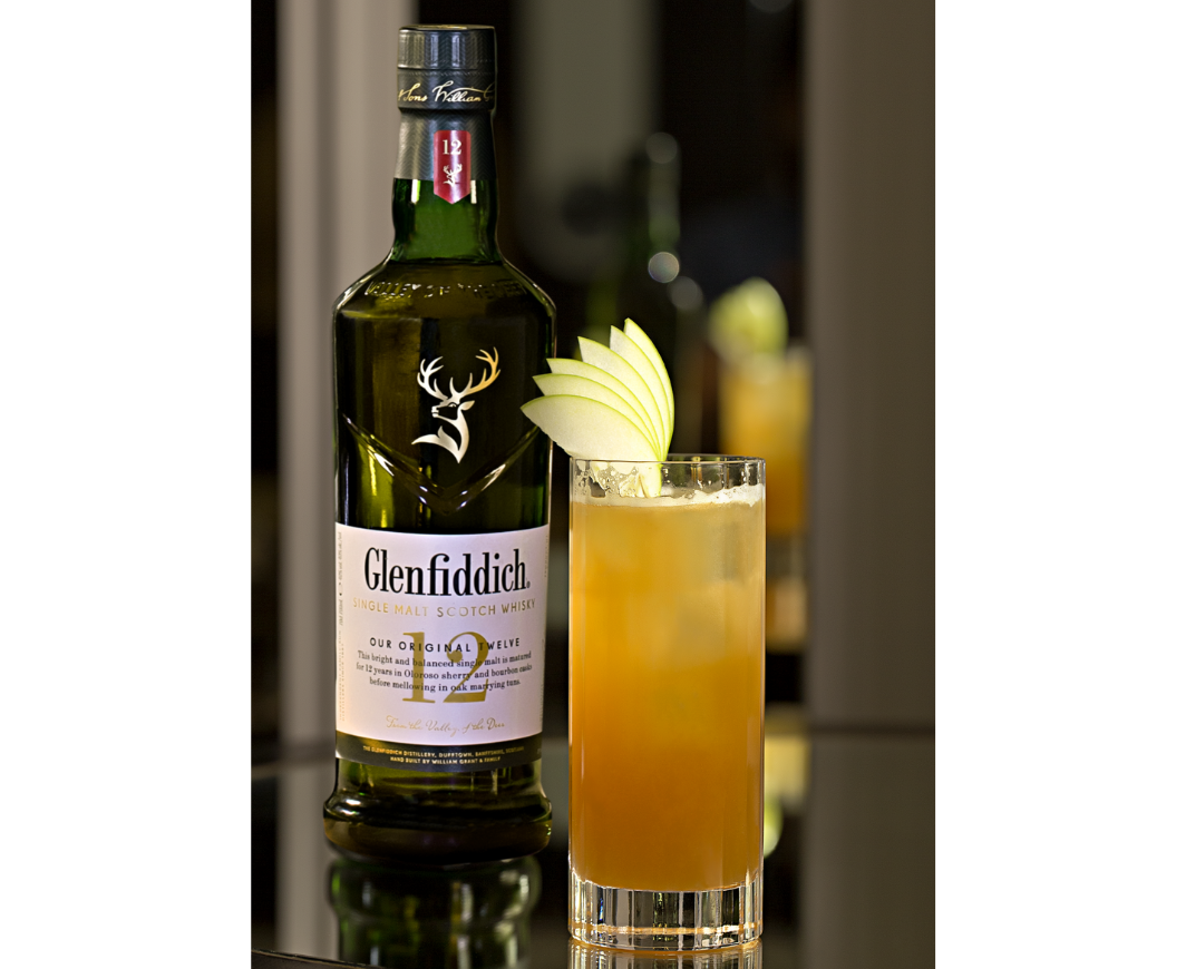 Eine Flasche Glenfiddich 12 Jahre neben einem Glen Fizzy Cocktail in einem Highball Glas mit Apfelscheiben garniert