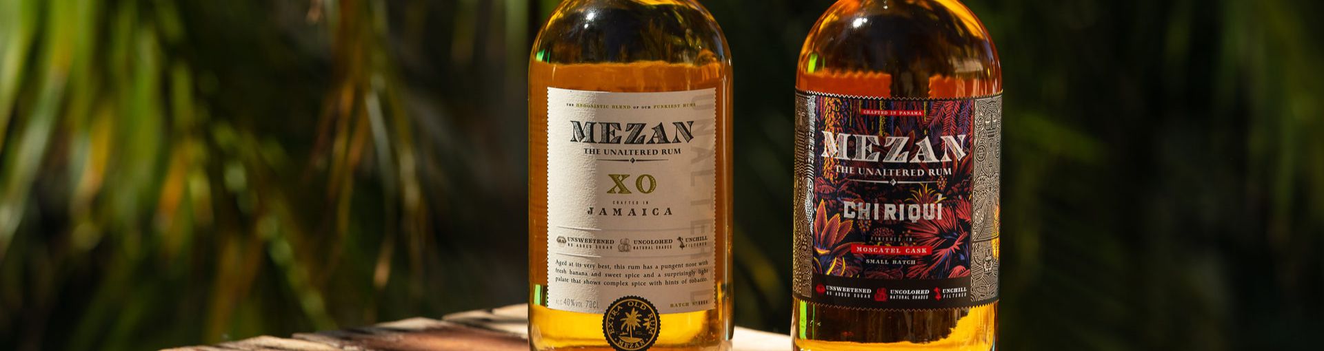 2 Flaschen Mezan Rum auf einer Holzkiste mit tropischem Hintergrund