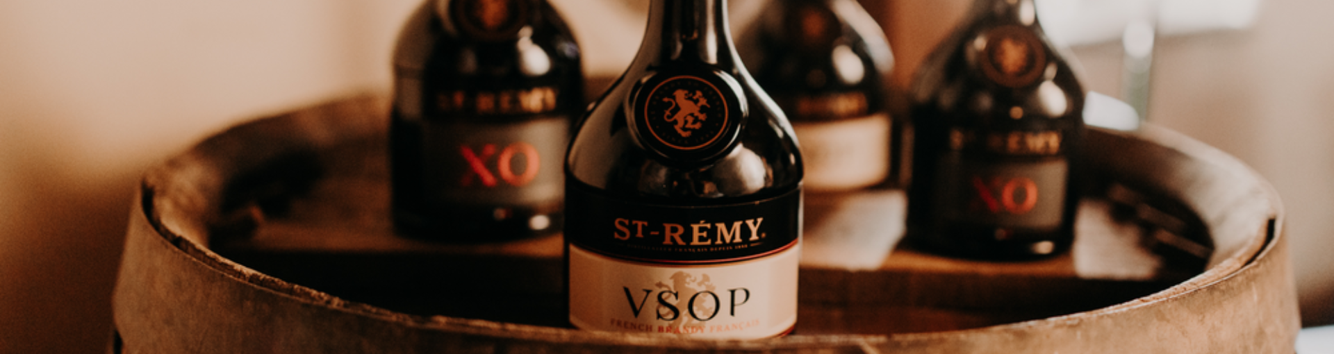 Jeweils 2 Flaschen St. Remy VSOP und St. Remy XO auf einem Holzfass