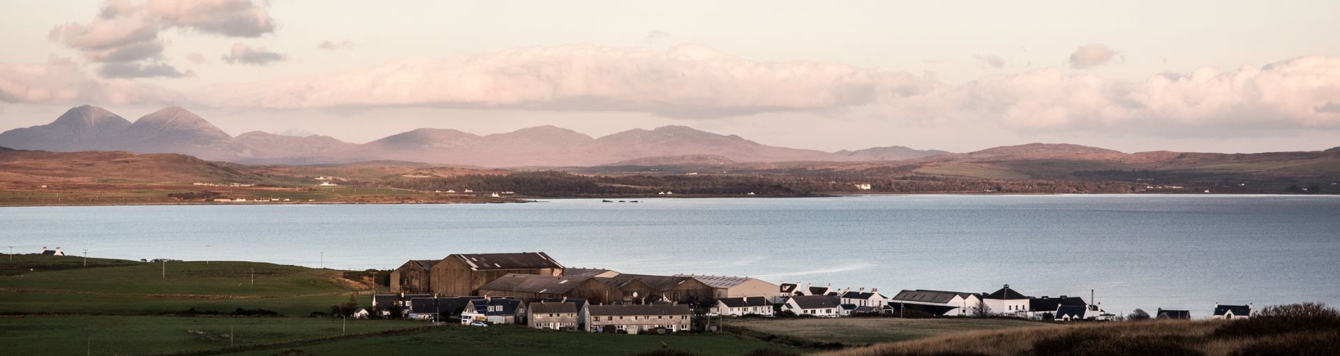 Bruichladdich Distillery an einem See mit Bergen und grüner Landschaft im Hintergrund