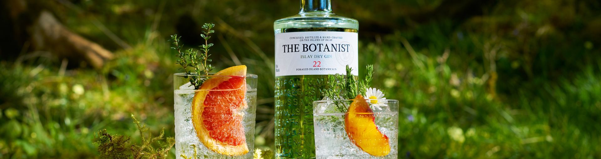 Botanist Gin Flasche mit zwei Gin Tonic Glaser auf einer Kräuterwiese