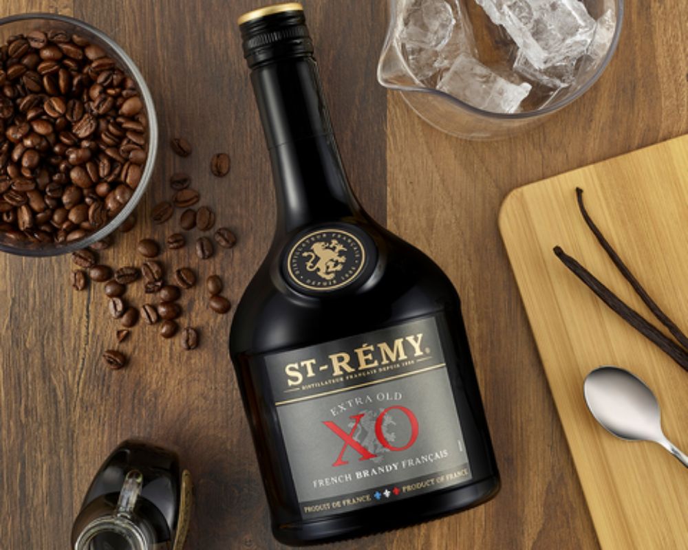 St. Remy XO Flasche liegt am Holztisch mir Kaffeebohnen und Vaille