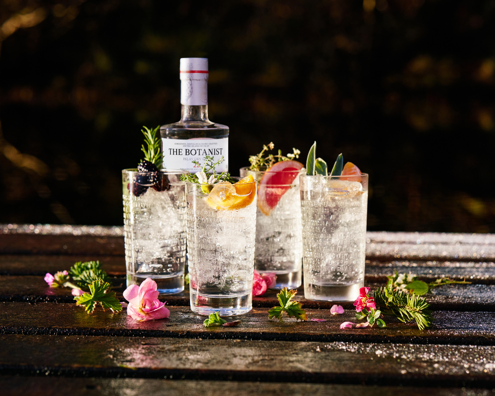 Botanist Gin Flasche steht am TIsch, davor Gläser mit Gin Longdrinks und Blüten gefüllt
