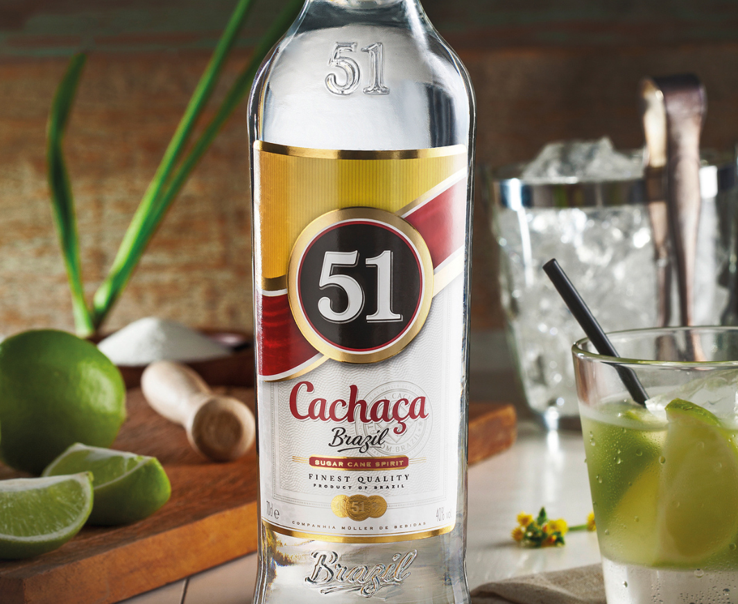 Flasche Cachaca 51 steht mit einem Glas Caipirinha am Tisch, daneben liegen Limetten