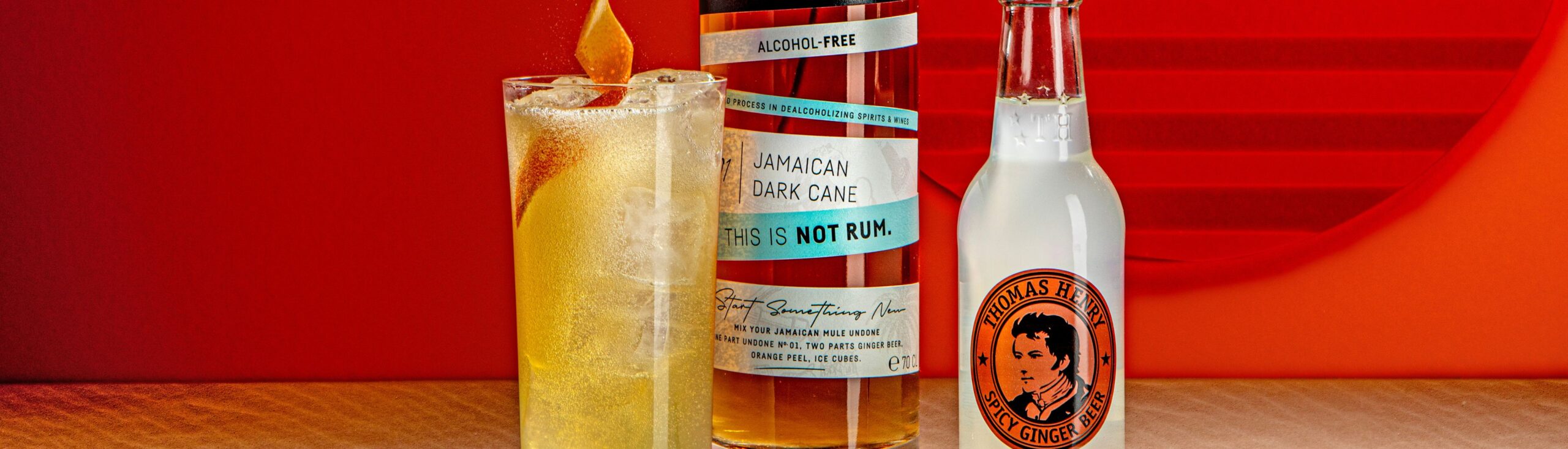 Undon not Rum mot Thomas Henry Flasche und Drink vor einem roten Hintergrund