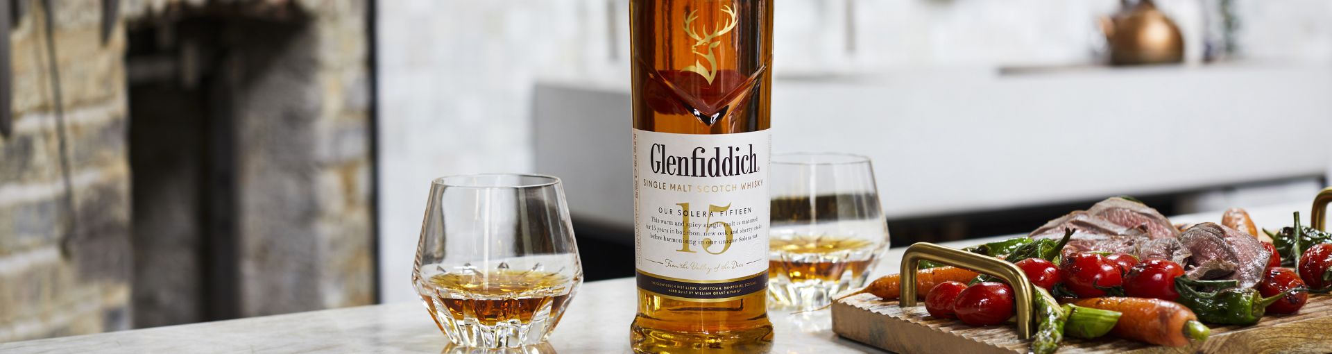 Glenfiddich 15 Jahre Flasche stehet auf einem Tisch, daneben zwei gefüllte Tumbler Gläser