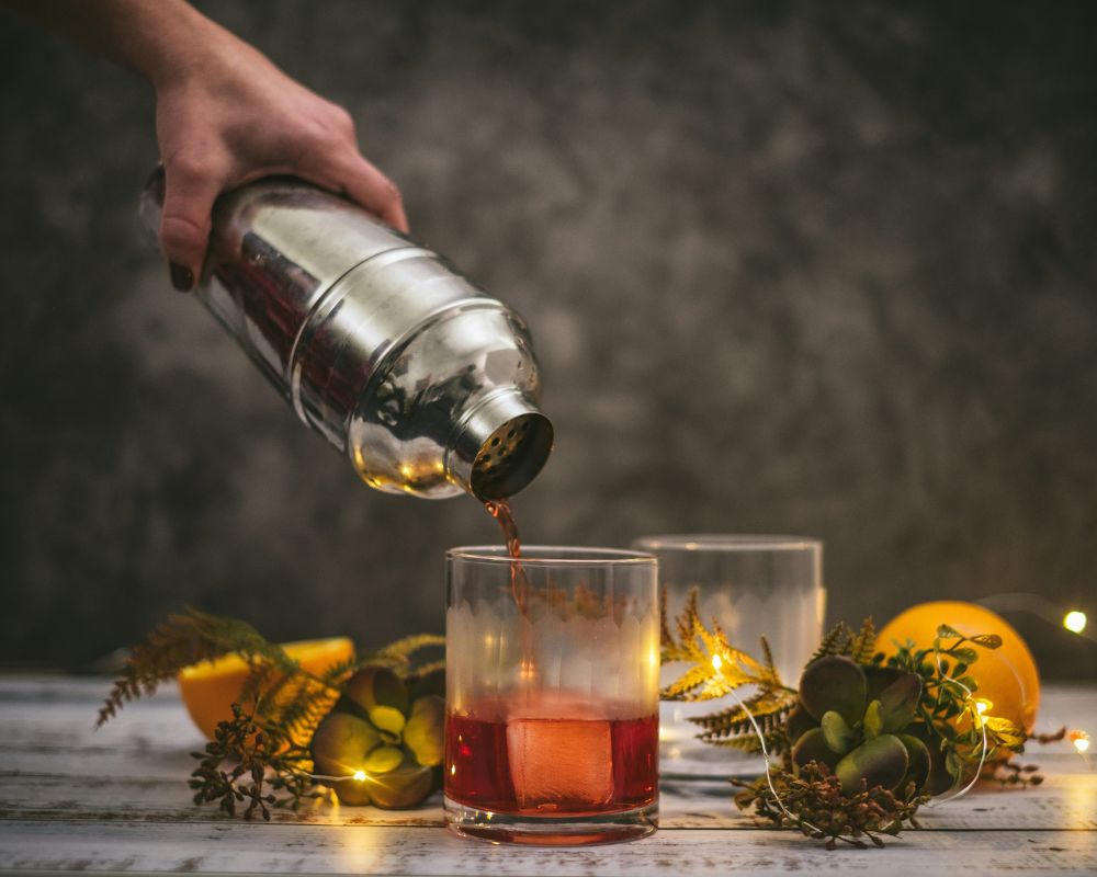 Bartneder leert Drink aus einem Shakerin ein Tumblerglas.